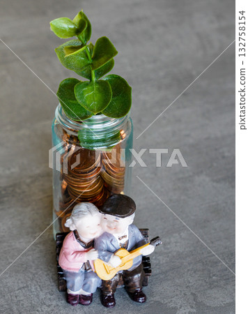 Symbolic money tree with coin jar and elderly couple figurines representing financial growth 132758154