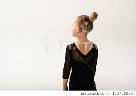 Little girl in black latin dance dress performing graceful pose with cochlear implant. Copy space. Overcoming hearing loss through movement, inclusion, and confidence in art and rhythmic self Little girl in black latin dance dress performing graceful pose with cochlear implant. Copy space. Overcoming hearing loss through movement, inclusion, and confidence in art and rhythmic self 132758250