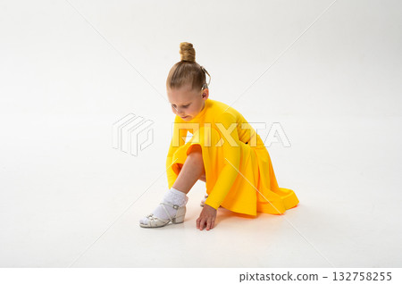 Little dancer with cochlear implant adjusting shoe on white floor. Copy space. Inclusion, discipline, and awareness of hearing technology in early childhood art. 132758255
