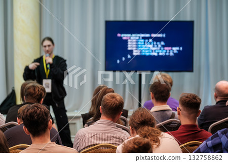 Presenter speaks to audience at tech conference with coding screen in background Presenter speaks to audience at tech conference with coding screen in background 132758862
