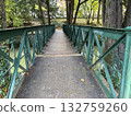 Old-fashioned wooden and iron pedestrian bridge with decorative railings over river in park, autumn scenery small town landscape, peaceful relaxing calm natural atmosphere with autumn leaves on path 132759260
