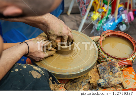 Close-up of potters and a boy hands forming ceramic bowl on spinning wheel during craft workshop. Concept of pottery, creativity, traditional handmade clay art 132759387