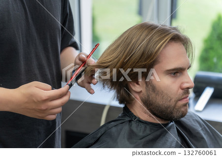 A hairdresser uses scissors and a red comb to give a haircut to a male client A hairdresser uses scissors and a red comb to give a haircut to a male client 132760061
