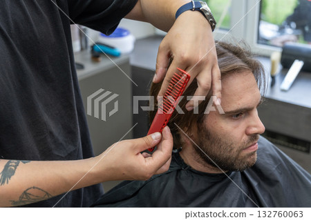 A hairdresser uses scissors and a red comb to give a haircut to a male client A hairdresser uses scissors and a red comb to give a haircut to a male client 132760063