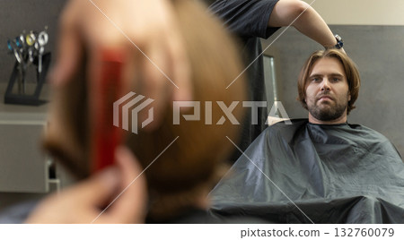 A hairdresser cuts a male client's long brown hair in a barbershop 132760079
