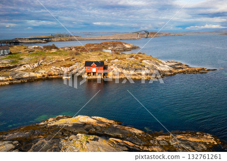 Tiny house on a rocky islet embraced by expansive fjord waters and steep mountain slopes, capturing the serene yet powerful natural beauty of coastal Norway. 132761261