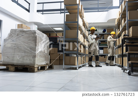 Black female worker handling orders and supply package shipments, managing goods in a depot warehouse. Distribution products arranged on racks ready for delivery, import export. Black female worker handling orders and supply package shipments, managing goods in a depot warehouse. Distribution products arranged on racks ready for delivery, import export. 132761723