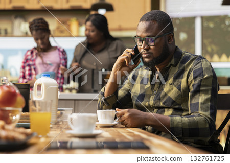 African american dad on a phone call for work during breakfast meal at home, interrupting family bonding time and morning routine to answer important calls. Father neglecting his children. 132761725