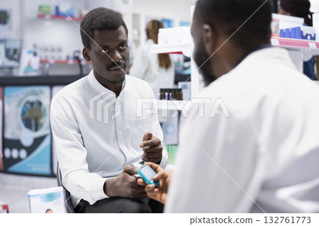 Black pharmacist using glucometer for sugar level measurements, checking the insulin levels and ensuring diabetic care in busy drugstore space. Specialist does health consultation. 132761773