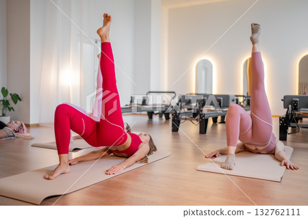 Pilates women performing inverted leg raises, pair of women practicing inverted leg raises with focus on the buttocks Pilates women performing inverted leg raises, pair of women practicing inverted leg raises with focus on the buttocks 132762111
