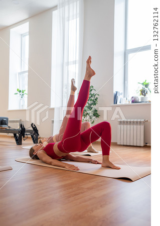 Pilates women performing inverted leg raises, pair of women practicing inverted leg raises with focus on the buttocks Pilates women performing inverted leg raises, pair of women practicing inverted leg raises with focus on the buttocks 132762114