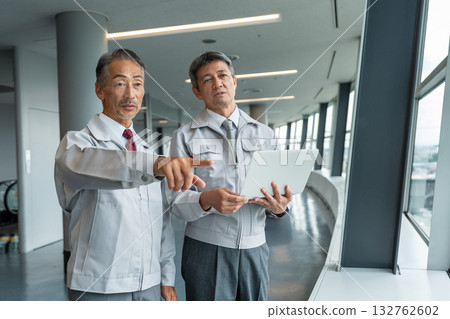 一名身穿工作服的男子和工地主管正在工地查看藍圖。 一名身穿工作服的男子和工地主管正在工地查看藍圖。 132762602