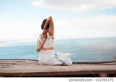 Woman practicing Cow Face Pose sitting on wooden Woman practicing Cow Face Pose sitting on wooden 132763175