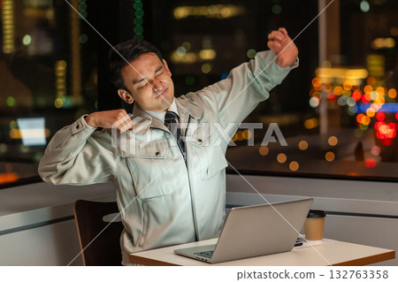 晚上,一位身穿工作服的男士在電腦前伸展身體 晚上,一位身穿工作服的男士在電腦前伸展身體 132763358