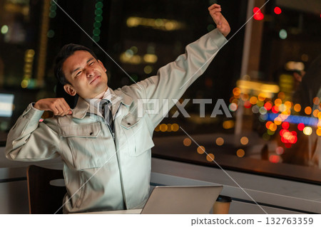 晚上，一位身穿工作服的男士在電腦前伸展身體 132763359