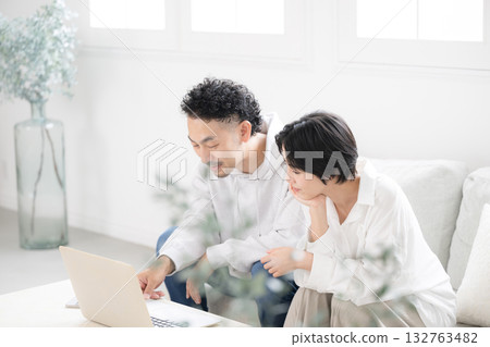 一對夫婦在綠植環繞的客廳使用電腦。他們正在搜尋有關搬家、保險等方面的資訊。 132763482