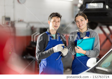 Car service manager discusses car repair problems with mechanic. He takes notes on paper 132763724