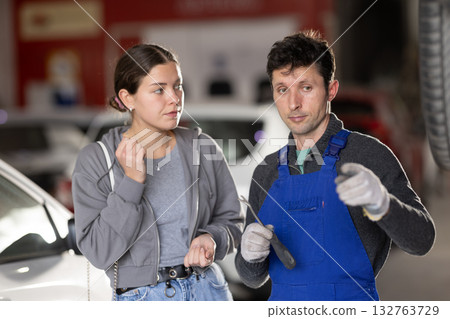 Man car mechanic talks with girl client in workshop and takes order. Man car mechanic talks with girl client in workshop and takes order. 132763729