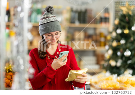 Teen girl customer at shop scan QR code on label at candies in gold package using phone camera 132763732