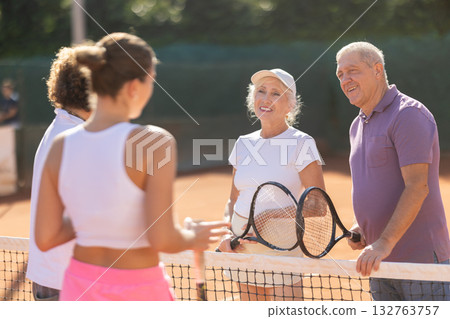 Group of friends or family spending time playing sports on tennis courts and talking during breaks 132763757