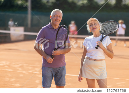 Elderly man and woman standing with rackets on court 132763766