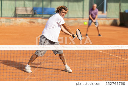 Sporty two men during doubles match on tennis court. Active sportsman hitting tennis ball with racket Sporty two men during doubles match on tennis court. Active sportsman hitting tennis ball with racket 132763768