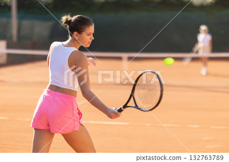 Back view of sporty young girl spending time playing tennis with racket and ball on tennis court Back view of sporty young girl spending time playing tennis with racket and ball on tennis court 132763789