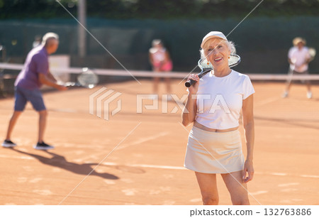 Elderly woman standing in front of tennis players Elderly woman standing in front of tennis players 132763886