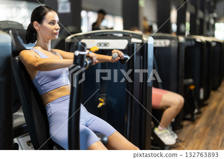 Sportive young girl training on chest press machine in gym 132763893