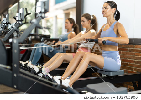 Sportive young girls training on cable row machine in gym Sportive young girls training on cable row machine in gym 132763900