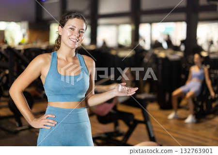 Positive young girl inviting visitors in well-equipped gym 132763901