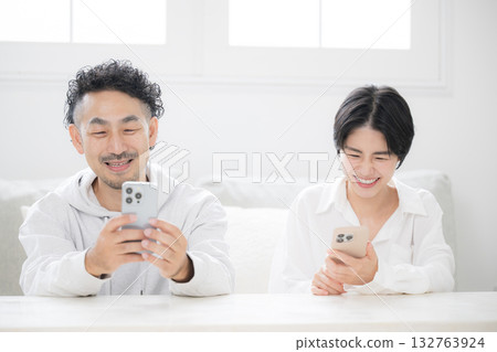 A middle-aged smiling couple looking at a smartphone in the living room 132763924