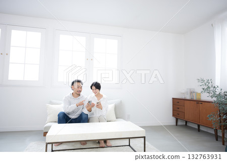 A middle-aged smiling couple looking at a smartphone in the living room A middle-aged smiling couple looking at a smartphone in the living room 132763931