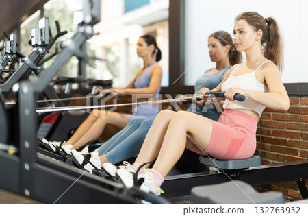 Women are engaged on a rowing machine 132763932