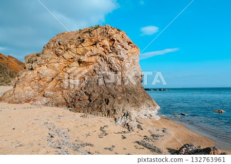Rocky cliff on a sandy beach at Shamora Bay, Cape Zelyony, Vladivostok. Clear blue sea and bright sky create a calm summer coastal background. 132763961