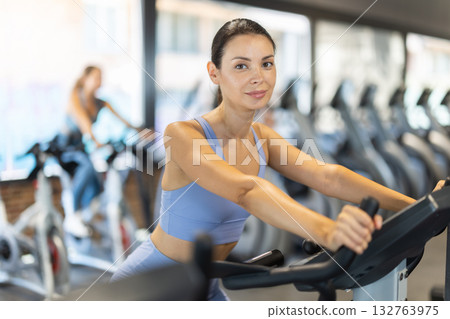 Smiling young girl doing spin bike exercises in well-equipped gym 132763975