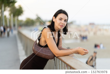 Young woman is leaning on parapet, looking towards sea. 132763978