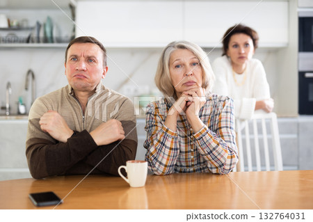 Angry middle-aged man and old woman sitting at the kitchen-table Angry middle-aged man and old woman sitting at the kitchen-table 132764031