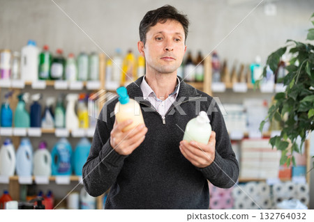 Among shop windows, man buyer leisurely examines goods and chooses liquid hand soap 132764032