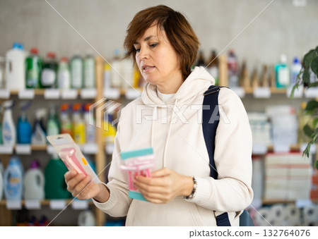 Woman carefully selects razor for shaving in the household goods department of supermarket 132764076