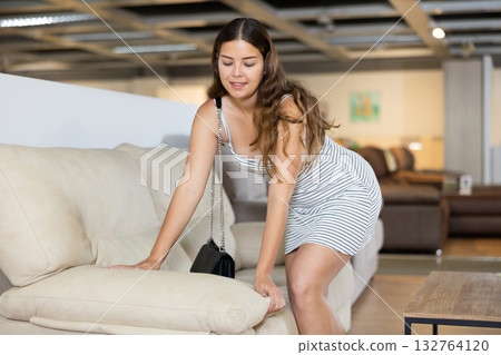 Young woman carefully examines sofa before buying and checks elasticity of surface with hand 132764120
