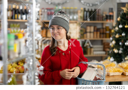 Female shopper with grocery cart attentively choosing fresh food in grocery supermarket for Christmas celebration 132764121
