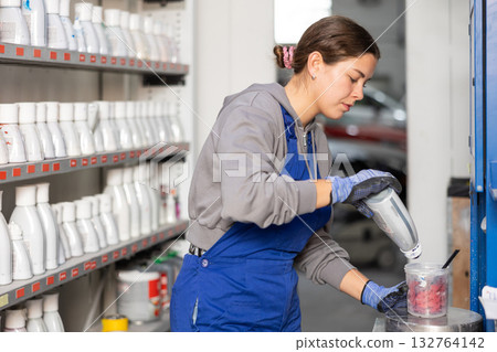 Girl colorist selects paint color by mixing different paint colors for subsequent painting of car in car service center Girl colorist selects paint color by mixing different paint colors for subsequent painting of car in car service center 132764142