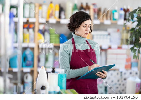 Middle-aged woman taking record of inventory in household store Middle-aged woman taking record of inventory in household store 132764150