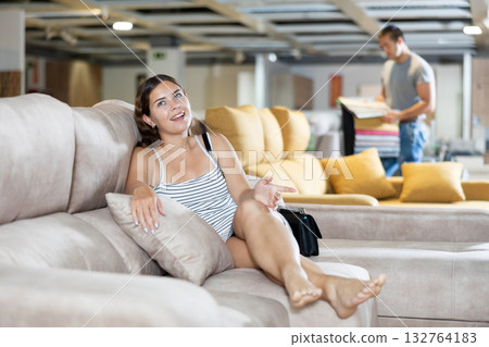 In furniture store,young girl is sitting on sofa with ottoman 132764183