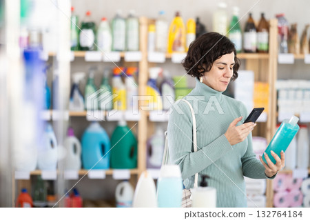Middle-aged woman scanning QR-code on shampoo at department store Middle-aged woman scanning QR-code on shampoo at department store 132764184
