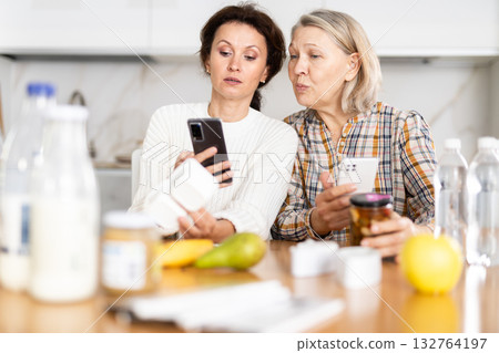 Adult daughter and elderly mother scan barcode on food package together using smartphone 132764197