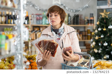 Female shopper with cart of groceries buys jamon in supermarket Female shopper with cart of groceries buys jamon in supermarket 132764215