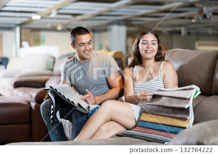 In exhibition hall,couple sat down on brown sofa and keep sets of upholstery material samples 132764222