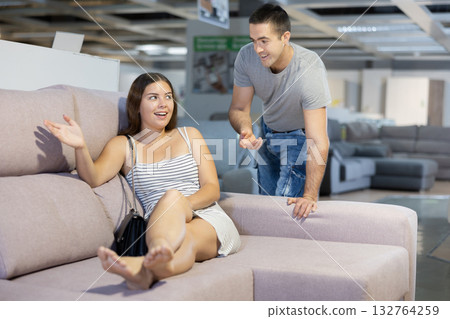 Couple chooses furniture in store.Wife is sitting on sofa,husband is standing next to her 132764259